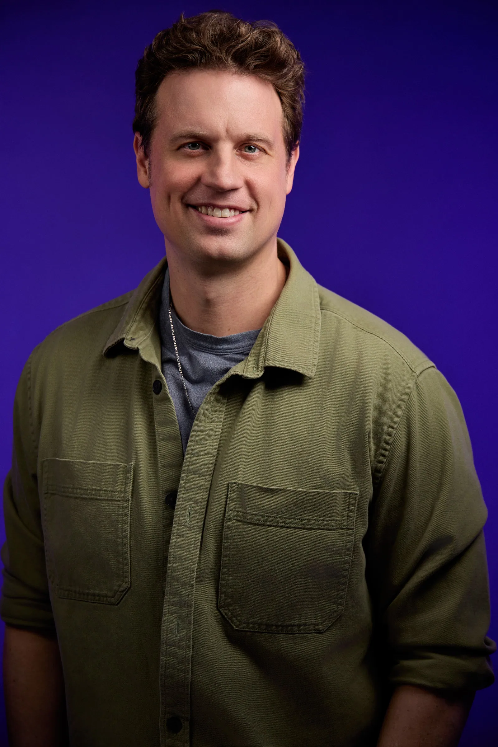 portrait of a man smiling in a green shirt with a purple background