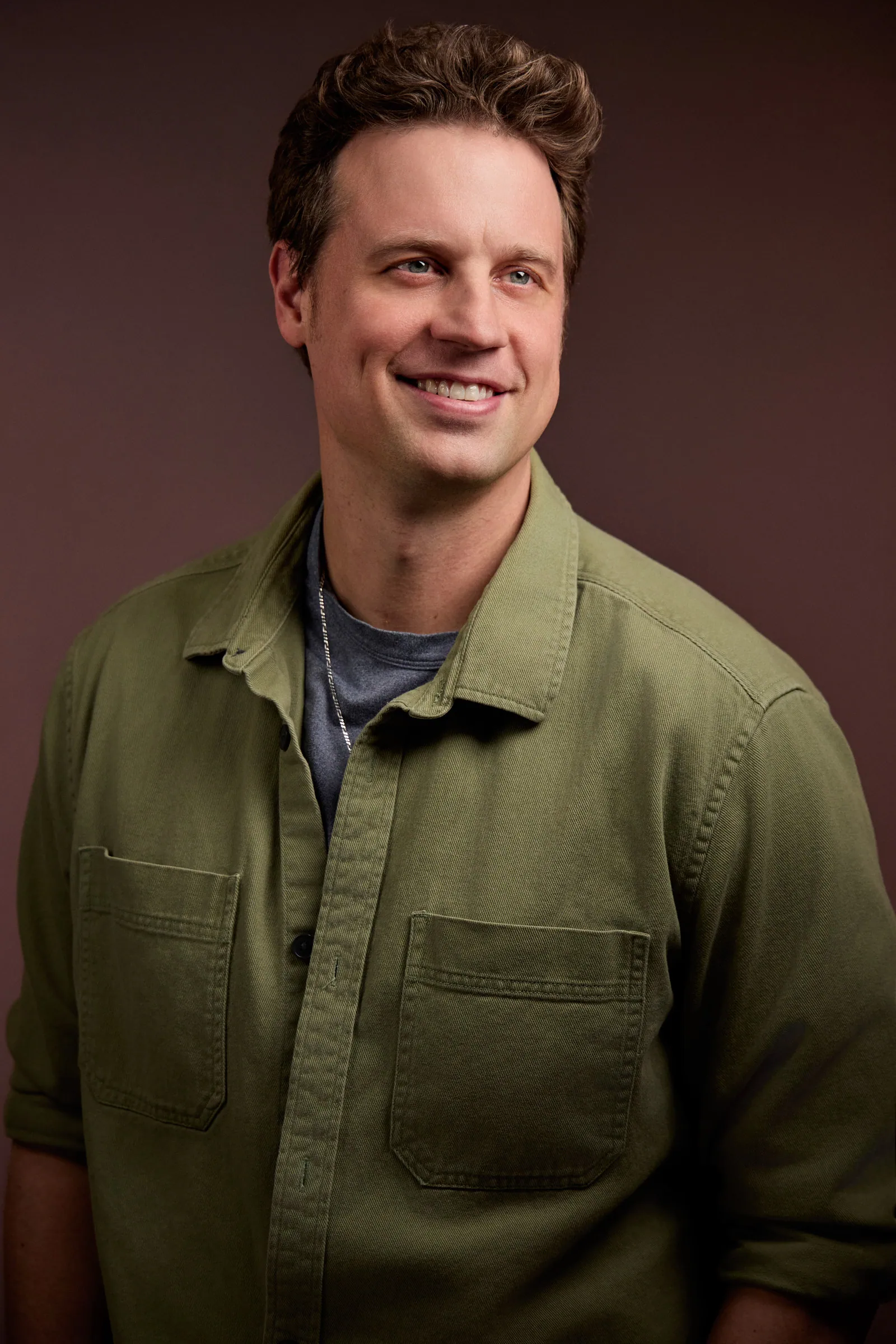 portrait of a man in a green shirt smiling while looking away from camera
